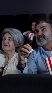 Olgun çift tereyağlı patlamış mısır paylaşırken ve birlikte gülerken loş aydınlatılmış tiyatroda gece sineması gösteriminin tadını çıkarıyor.