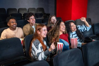 Gençler sinemada film izlerken, patlamış mısır yerken ve gülerken eğleniyorlar.