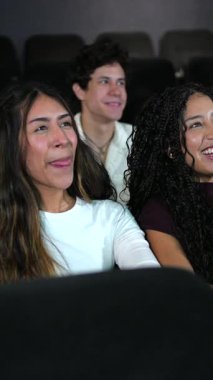 Üç boyutlu gözlük takan bir grup genç arkadaş loş ışıklı sinema salonunda birlikte film izlerken kahkaha ve heyecan paylaşıyorlar.