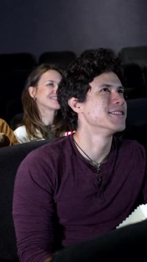 Genç yetişkinler karanlık sinema salonunda birlikte oturup patlamış mısırın tadını çıkarırken romantik bir anı paylaşıyorlar ve üç boyutlu film gösterimini izliyorlar.