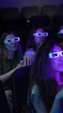 Farklı arkadaş grupları 3D gözlük takıyor, sinemada film izliyor ve patlamış mısır yiyor.