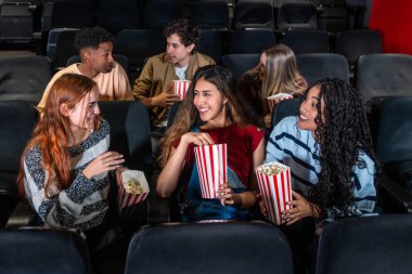 Neşeli çoklu etnik arkadaşlar, sıcak bir sinemada birlikte film izlerken patlamış mısırın tadını çıkarıyor, kahkahalarını ve gülümsemelerini paylaşıyor.