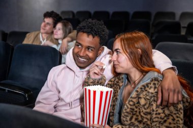 Sinemada film izlerken patlamış mısırlarını paylaşan mutlu, çok ırklı bir çift.