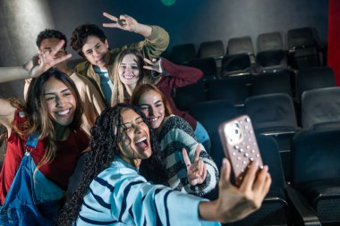 Sinema veya disko partisinde selfie çeken, zafer işaretleri yapan ve eğlenen bir grup neşeli genç arkadaş.