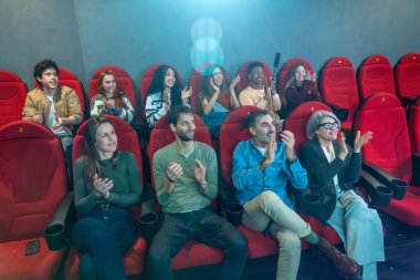 Çeşitli bir grup insan sinemada alkışlıyor ve birlikte bir filmden zevk alıyorlar. Heyecan ve minnettarlıkla dolu canlı bir atmosfer yaratıyorlar.