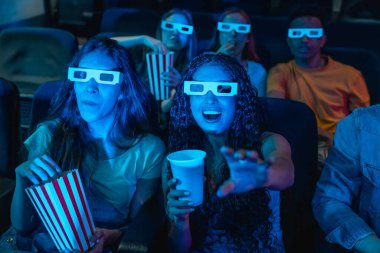 Genç insanlar 3D gözlük takıyor sinemada film seyrediyor, patlamış mısır yiyor ve gazoz içiyor, birlikte eğleniyorlar.