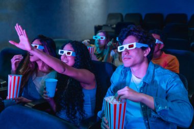 Üç boyutlu gözlük takan bir grup genç sinemada eğleniyor, patlamış mısır yiyor ve eğleniyor.