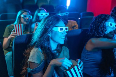 Bir grup arkadaş 3D gözlük takıyor, film izliyor, patlamış mısır yiyor, sinemada birlikte vakit geçiriyorlar.