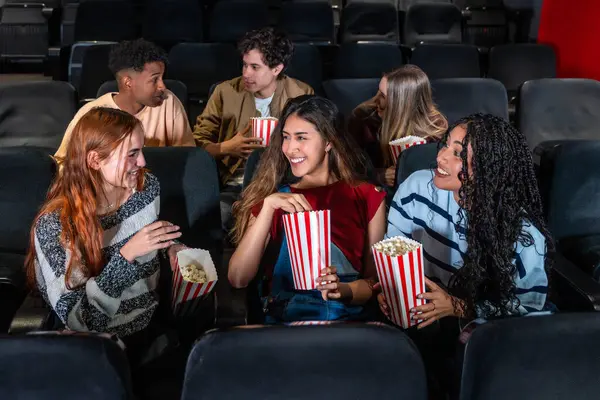 Neşeli çoklu etnik arkadaşlar, sıcak bir sinemada birlikte film izlerken patlamış mısırın tadını çıkarıyor, kahkahalarını ve gülümsemelerini paylaşıyor.