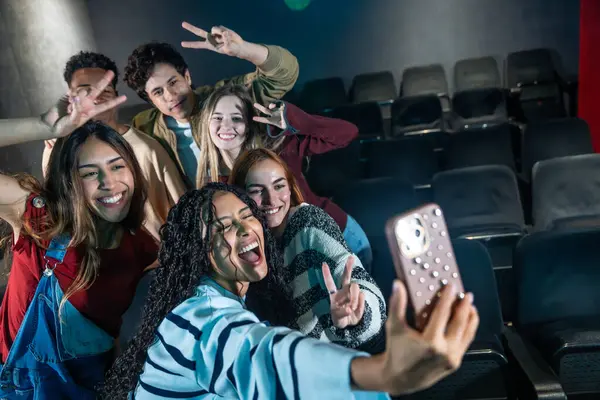 Sinema veya disko partisinde selfie çeken, zafer işaretleri yapan ve eğlenen bir grup neşeli genç arkadaş.