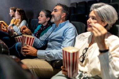 Bir grup arkadaş, sıcak bir sinemada heyecan verici bir film izlerken gülüp patlamış mısırın tadını çıkarıyorlar.