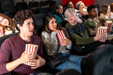 Gençler ve yetişkinler korku ve gerilim yaşarken sinemada korku filmi izleyip patlamış mısır yiyorlar.