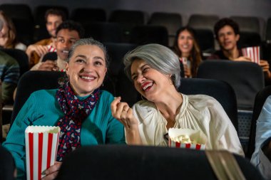 Sinemada film izlerken gülen ve patlamış mısır yiyen iki neşeli son sınıf kadını birlikte neşeli bir anı paylaşıyorlar.