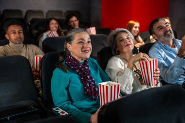 Sinemada film izleyen, patlamış mısır yiyen ve 3D gözlük takan bir grup insan.