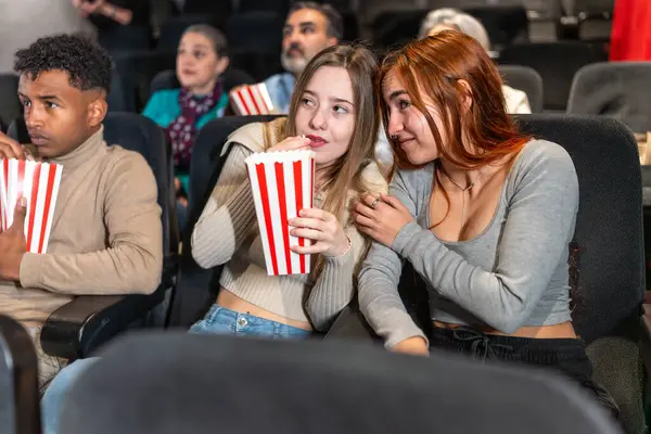 İki arkadaş sinemada başkalarıyla çevrili bir film izlerken fısıldayıp patlamış mısır yiyorlar.