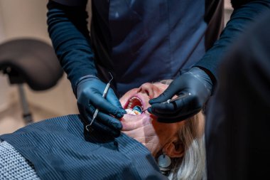 Diş hekimi siyah eldiven giyiyor. Son sınıf bir kadının dişlerini muayene ediyor. Kontrol sırasında dişçi koltuğunda yatıyor.