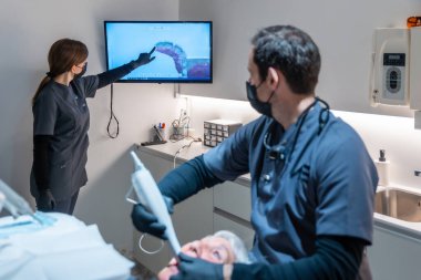 Diş hekimleri, kıdemli bir hastanın teşhis ve tedavisini tartışırken monitörde dijital röntgen filmini analiz ediyorlar.