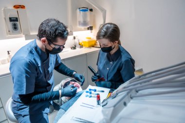 Diş hekimi ve asistanı modern bir diş kliniğinde diş beyazlatma prosedürü uyguluyor, ağız sağlığı ve daha parlak bir gülümseme sağlıyor.