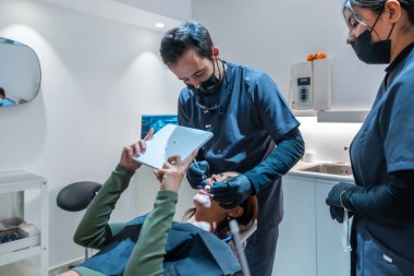 Diş beyazlatma sonuçları, modern bir diş sağlığı kliniğinde bir diş asistanının yardımıyla dijital tablet kullanan bir hastaya gösteriliyor.