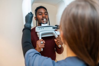 Diş hekimi modern bir diş kliniğinde erkek bir hasta için panoramik bir diş röntgeni hazırlıyor.