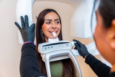 Dişçi, modern bir diş kliniğinde genç bir kadının diş röntgenini çekiyor ve en uygun tedavi için doğru teşhisi koyuyor.