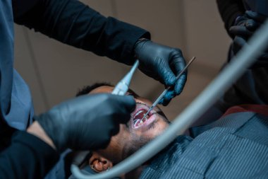 Modern diş sağlığı kliniğinde kontrol sırasında hastaların dişlerini diş aletleriyle muayene eden siyah eldivenler giyen bir dişçi.