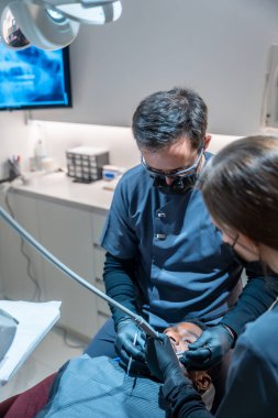 Diş hekimi ve diş hekimi asistanı, modern bir diş kliniğinde bir hastaya diş tedavisi uyguluyor.