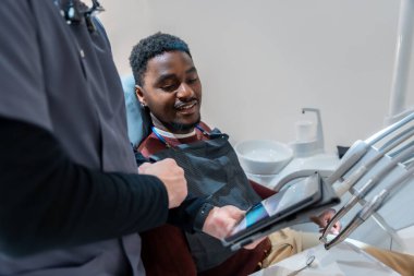 Modern bir diş kliniğinde muayene sırasında gülümseyen bir hastaya diş röntgeni gösteren bir diş hekimi.