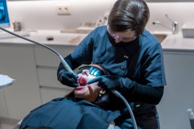 Diş hekimi modern bir diş kliniğinde diş beyazlatma prosedürü için özel ekipman kullanıyor. Ağız hijyeni ve daha parlak bir gülümseme sağlıyor.