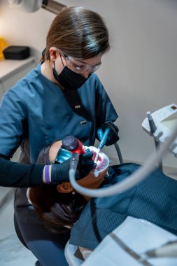 Diş hekimi, diş beyazlatma prosedürü için özel ekipman kullanır. Modern bir klinikte profesyonel diş bakımı gösterir.