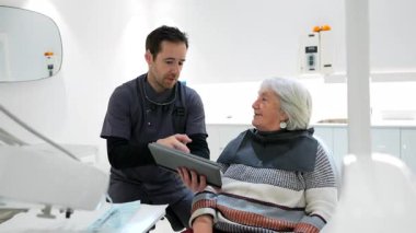 Deneyimli bir diş hekimi, modern diş sağlığı kliniğinde profesyonel tıbbi danışmanlık sırasında dijital tablet kullanıyor.