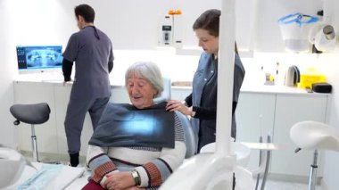 Modern bir klinikte dişçi ve hemşirenin de yardımıyla dişçi muayenesi için hazırlanan yaşlı bir kadın.