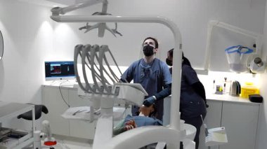 Deneyimli diş hekimi ve asistanı kapsamlı diş prosedürü uyguluyor. Gelişmiş tıbbi teknolojiyi el değmemiş, modern klinik ortamda kullanıyor.