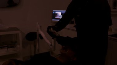 Diş hekimi modern diş kliniğinde beyazlatma işlemi sırasında hastanın dişlerine ultraviyole ışık uygular.