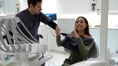 Modern, parlak klinik ortamında diş muayenesi sırasında tablet kullanan hastaların tedavi sonuçlarını inceleyen profesyonel dişçi