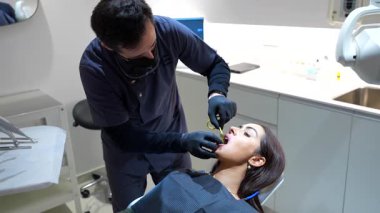 Profesyonel dişçi tam diş kontrolü yapıyor. Modern klinikte kadın hastaların röntgenlerini dikkatlice çekiyor.