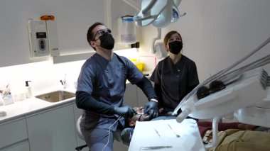 Profesyonel diş hekimi ve diş asistanı, modern klinik ortamında uzmanlaşmış diş donanımı kullanarak, hasta üzerinde işbirlikçi oral sağlık muayenesi gerçekleştiriyor.