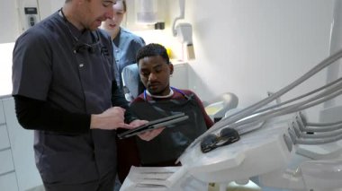 Diş sağlığı merkezindeki hastaya tablet hakkında bilgi veren diş hekimi, tedavi seçeneklerini ve diş bakımını tartışıyor