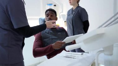 Modern, parlak diş sağlığı kliniğinde dijital tablet kullanan hastalara tıbbi bilgileri sunan profesyonel dişçi, ileri düzey sağlık teknolojisi ve hasta merkezli iletişimi gösteriyor