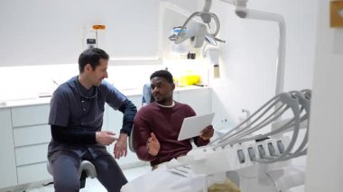 Modern diş sağlığı kliniğinde hasta danışmanlığı sırasında dijital tablette tıbbi tedavi detaylarını açıklayan profesyonel bir diş hekimi