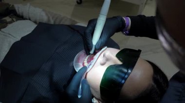 Profesyonel dişçi diş beyazlatma prosedürünü uyguluyor, modern klinik ortamında hastanın diş sağlığını dikkatlice tedavi ediyor.