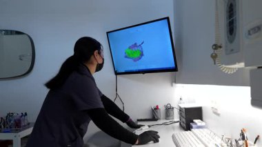 Yüz maskesi ve kalkan takan diş hekimindeki bir bilgisayarda 3 boyutlu röntgen taraması yapan bir diş hekimi.