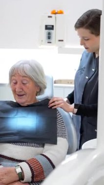 Diş hekimi, yaşlı bir kadını diş röntgenine hazırlar. İşlem sırasında rahat ve güvende olmasını sağlar.