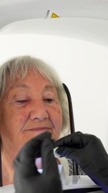 Diş hekimi yaşlı bir kadını 3 boyutlu diş taraması için hazırlıyor. Doğru görüntüleme için doğru konumu sağlıyor.