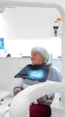 Deneyimli kadın hasta, dişçi koltuğunda yaslanıyor. Rutin sağlık kontrolleri sırasında uzman diş hekiminden kapsamlı bir ağız sağlığı hizmeti alıyor.