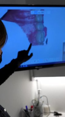 Diş hekimi, bir bilgisayar ekranındaki 3 boyutlu diş modelini göstererek teşhis ve tedavi planını açıklıyor.