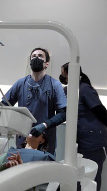 Modern, steril diş sağlığı kliniğindeki hastaya detaylı sözlü muayene ve tedavi uygulayan profesyonel dişçi ve diş asistanı