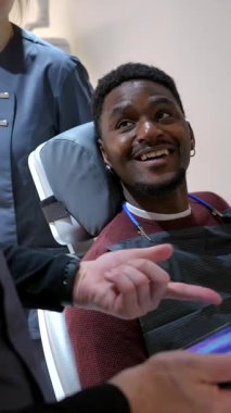 Genç adam dişçisiyle dişlerinin 3 boyutlu modelini gösteren tablete bakarak diş prosedürünü tartışıyor.