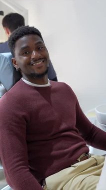 Rahatlamış Afrikalı Amerikalı erkek hasta diş muayenesi sırasında güvenle gülümsüyor, profesyonel sağlık muayenesi sırasında modern klinik koltuğunda rahatça oturuyor.