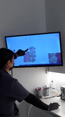 Diş hekimi dijital ekrandaki x ışını görüntüsünü göstererek modern klinikte diş tedavisine başlamadan önce hastaya teşhisi açıklar.